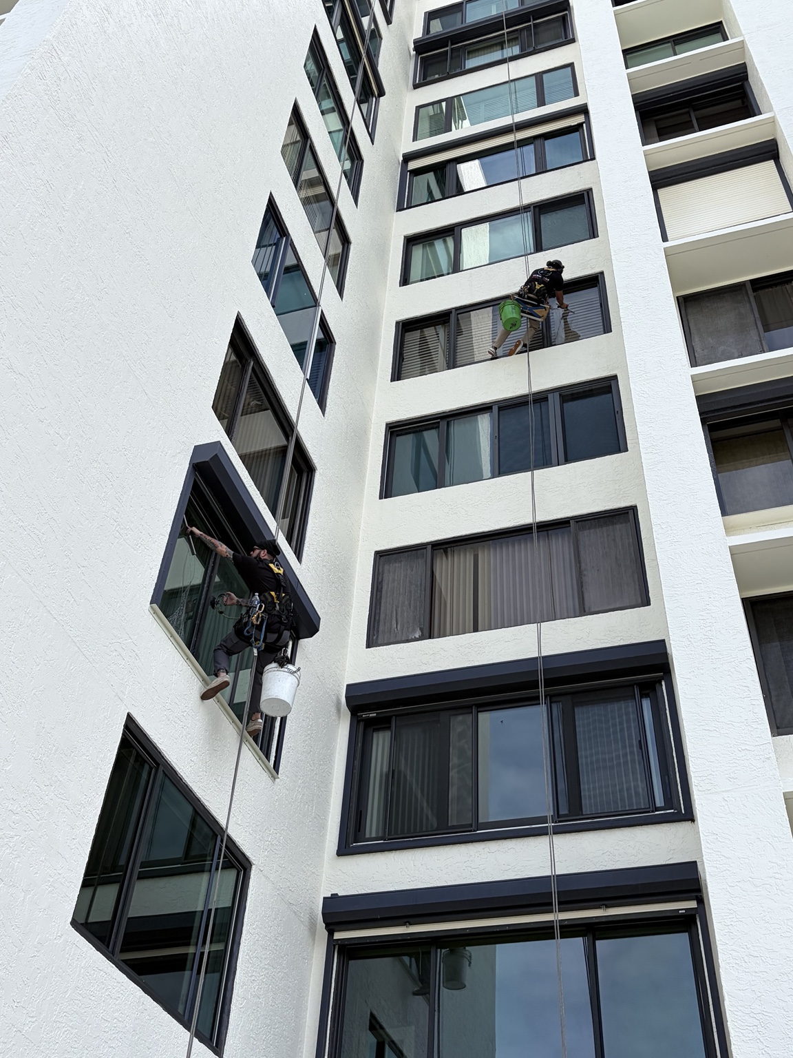 Two rope-access window cleaners working on a high-rise